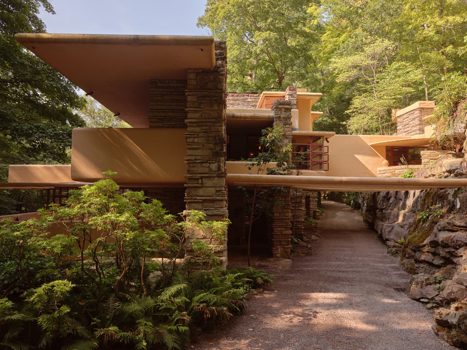 Fallingwater entry walkway with stacked stone piers and cantilevered concrete balconies amid ferns