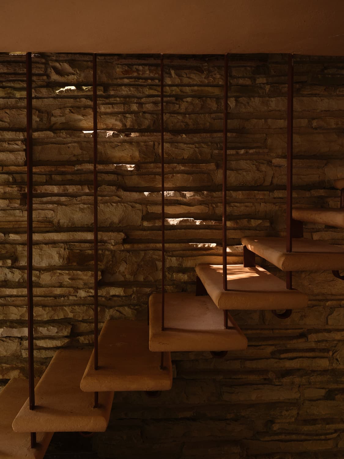 Floating concrete stair treads against stacked sandstone wall with light filtering through at Fallingwater