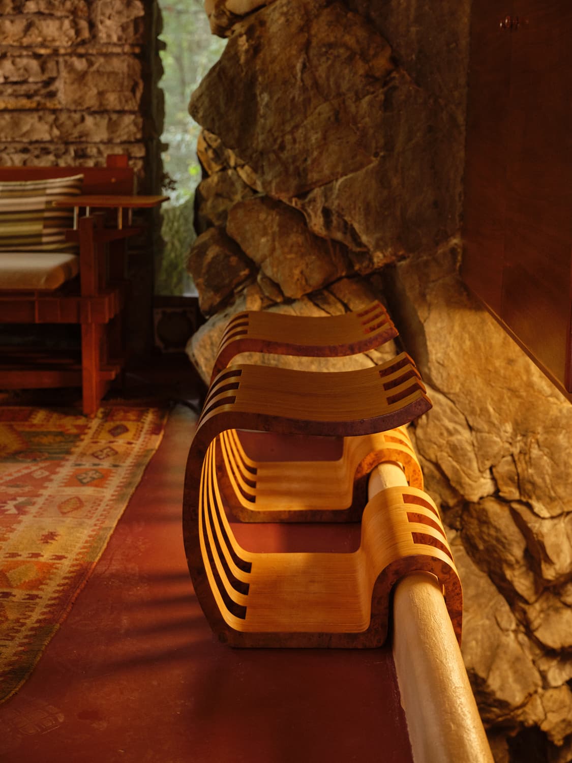 Sculpted laminated wood bench detail beside the stone fireplace inside Fallingwater