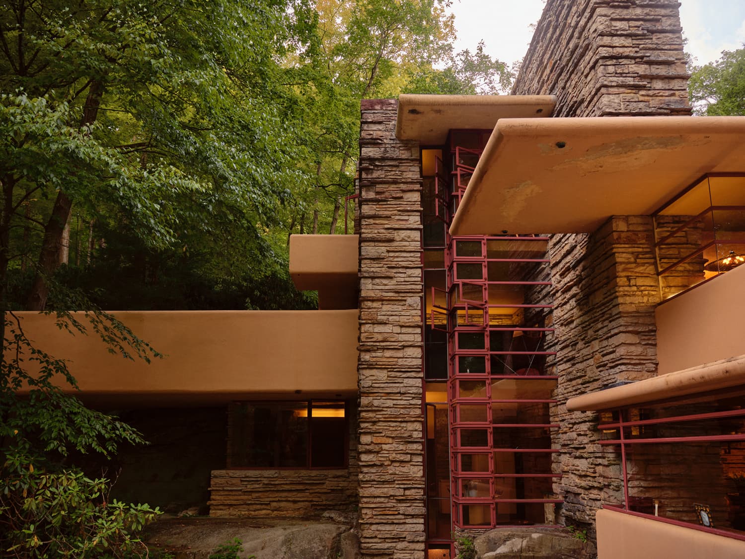Vertical stone tower and stacked cantilevers of Fallingwater with red steel window frames in the forest