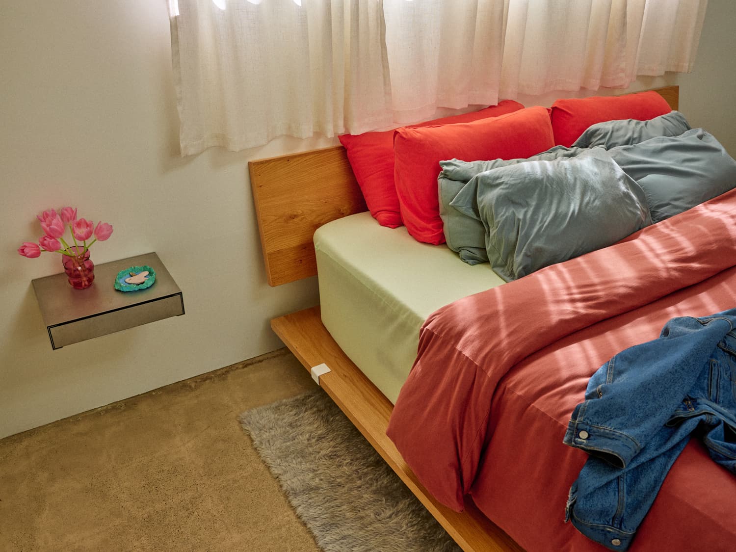Oak platform bed with coral and sage bedding beside a floating nightstand with tulips