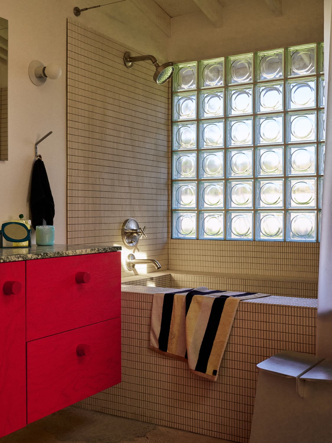 Retro tiled bathroom with glass block window, red vanity, and brass shower fixture