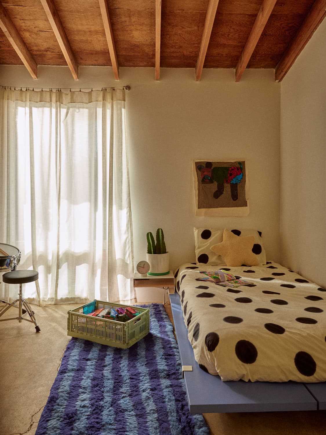 Kids bedroom with polka dot bedding, exposed beam ceiling, purple rug, and a drum set