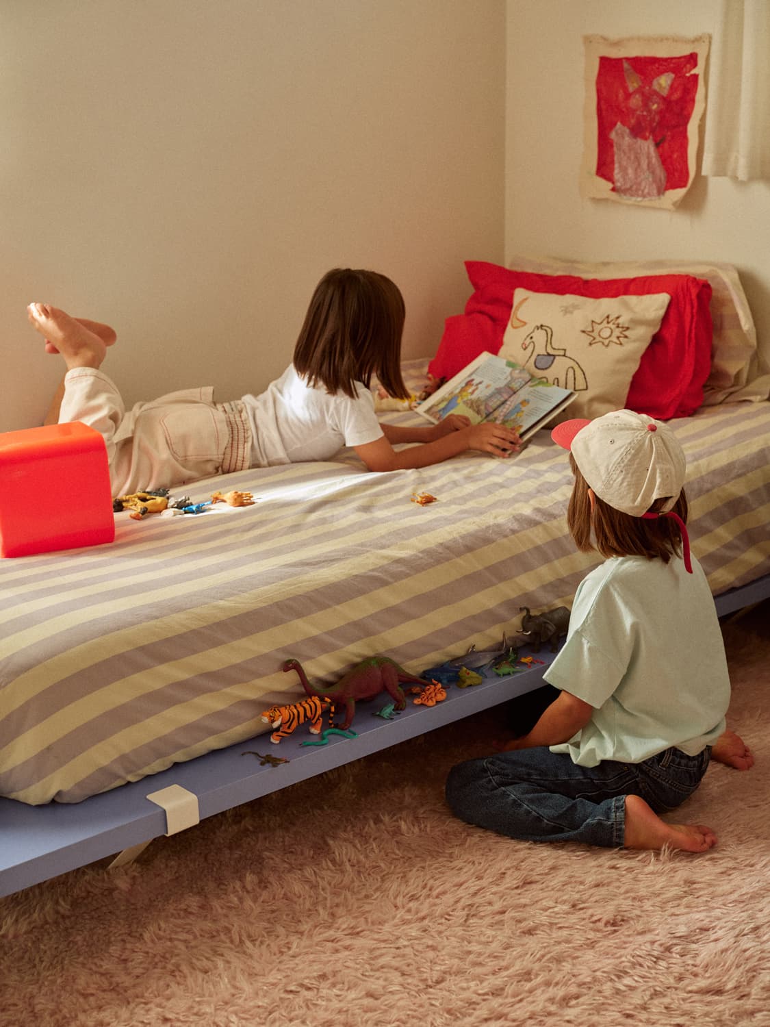 Two children reading and playing with toy dinosaurs on a striped bed in a cozy room