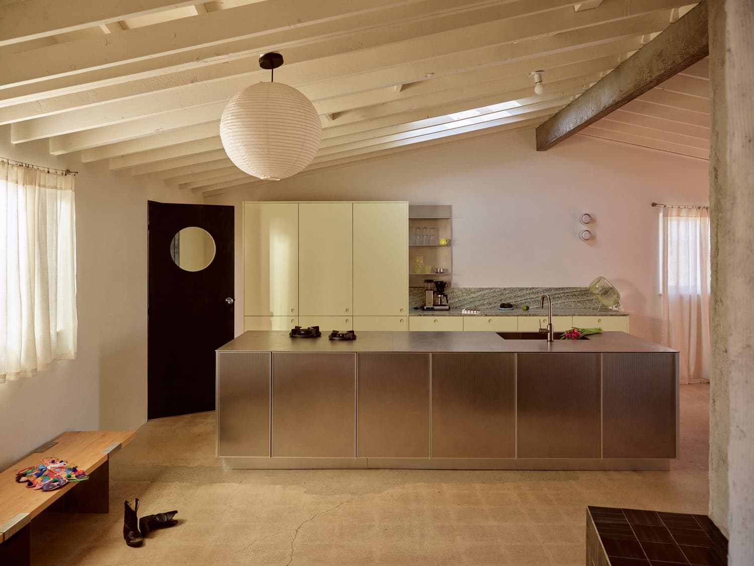 Modern kitchen with stainless island, yellow cabinetry, paper lantern, and concrete floors