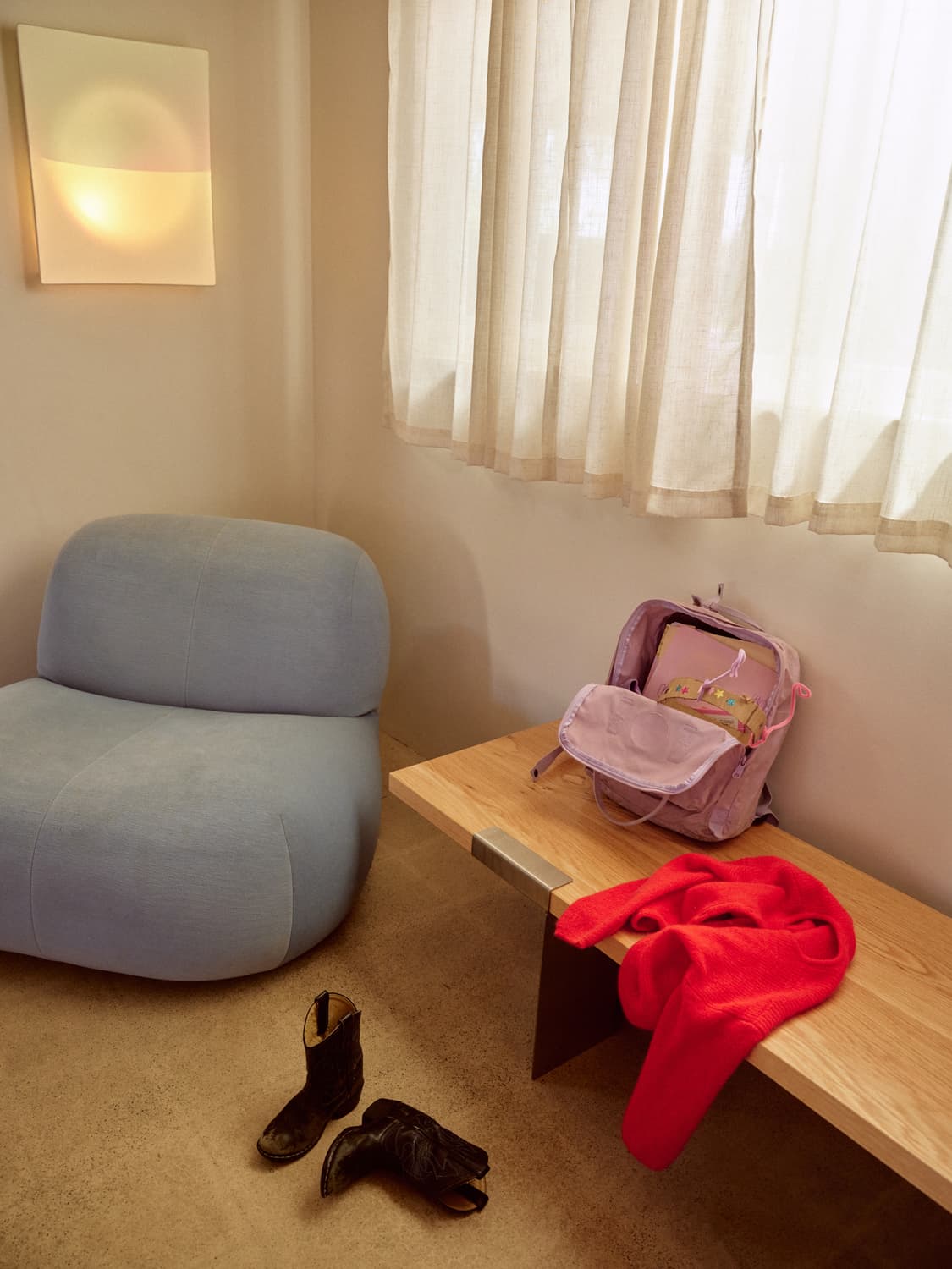 Light blue rounded chair beside an oak bench with a backpack and red sweater in an entryway