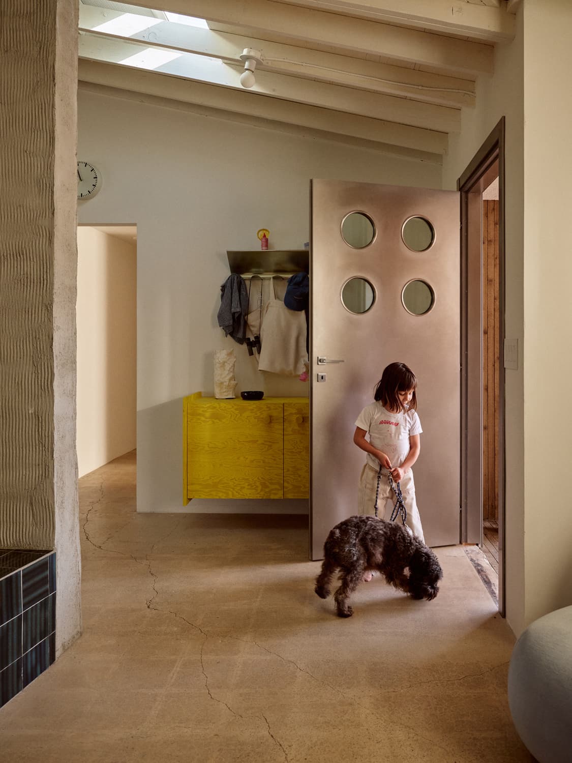Girl leashing a curly haired dog in a hallway with a pink door and yellow cabinet