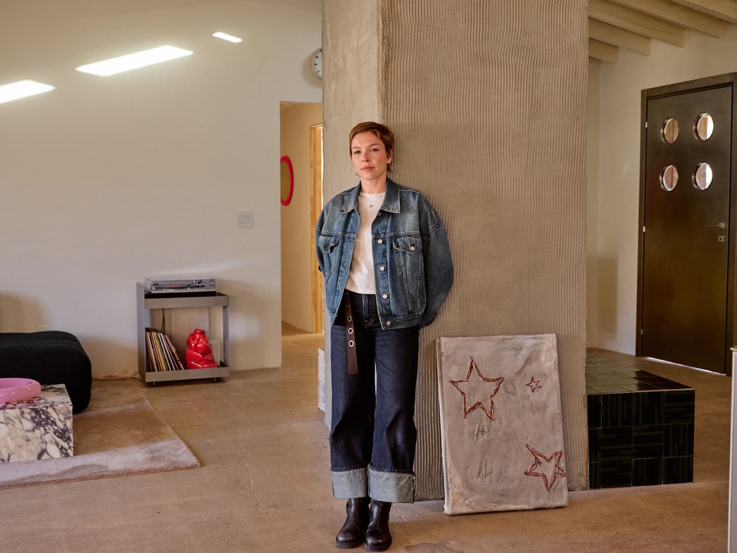 Bethany Brill in a denim jacket leaning against a concrete column in her open plan living room