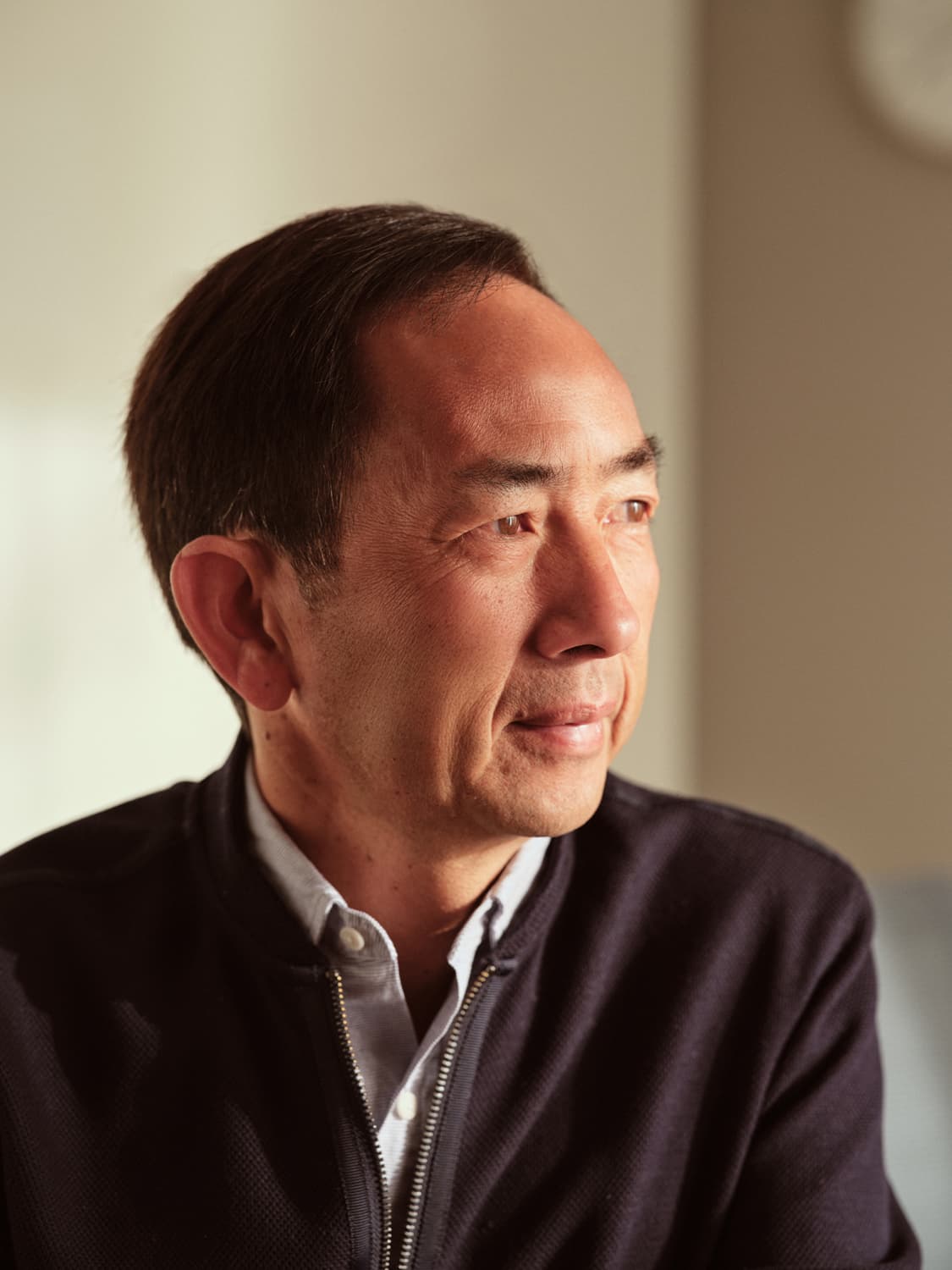Close-up portrait of a man in a dark zip jacket and light collar shirt gazing off camera in soft natural light