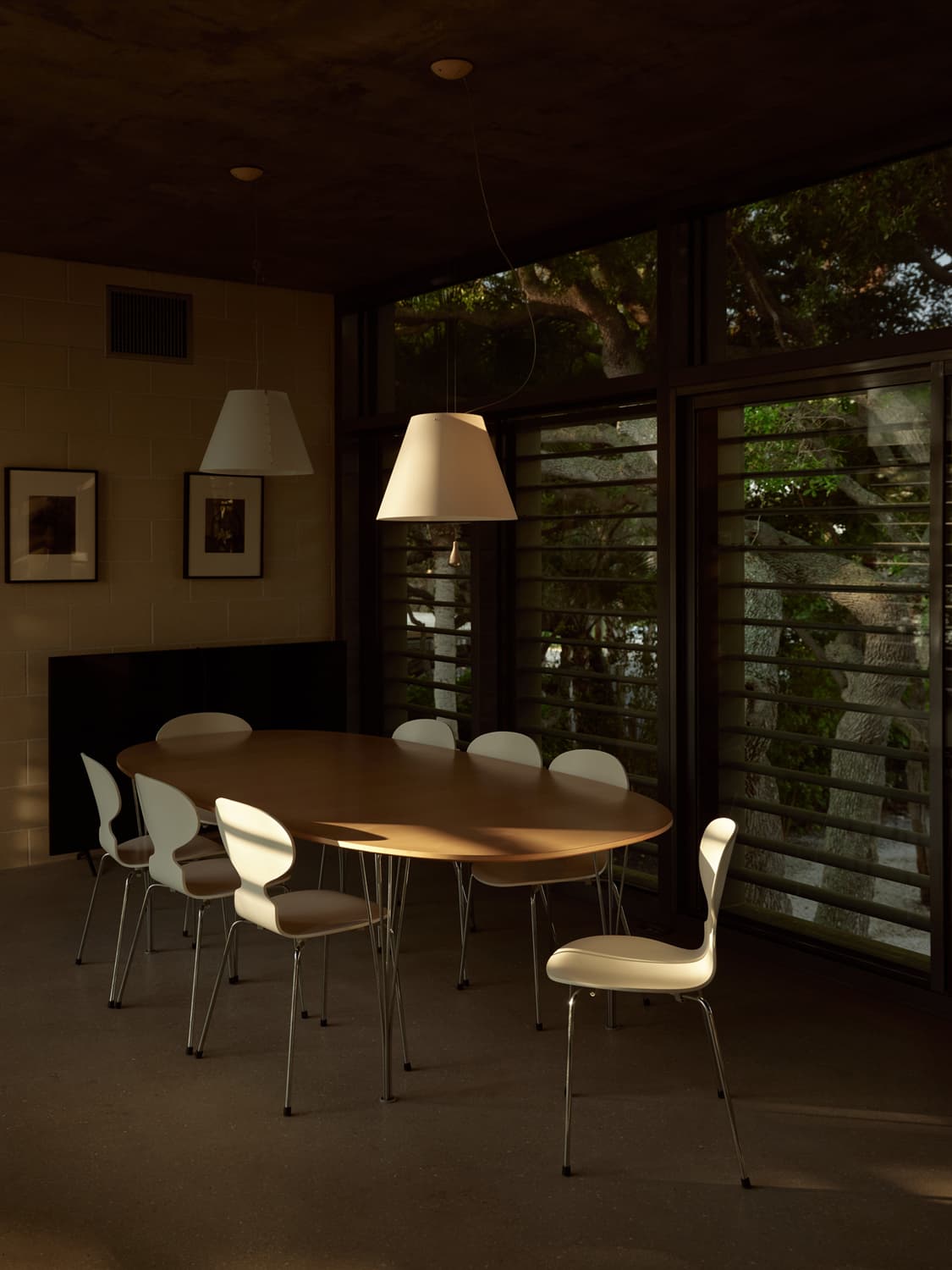 Dining room with oval table, white Ant chairs, pendant lights, and louvered windows at the residence