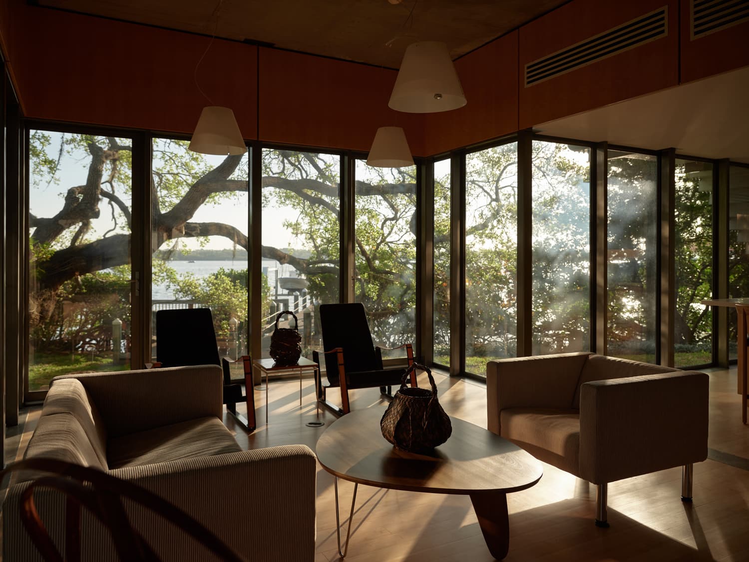 Corner living room with Noguchi coffee table, modern seating, and panoramic water views through glass