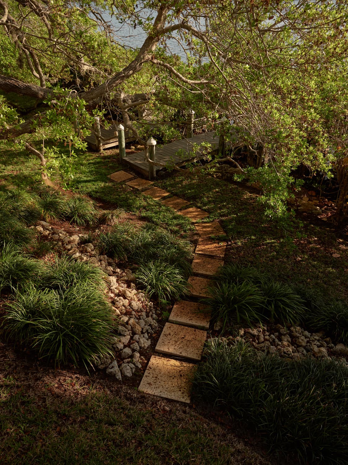Stepping stone path through lush tropical garden leading to a wooden bridge at the residence