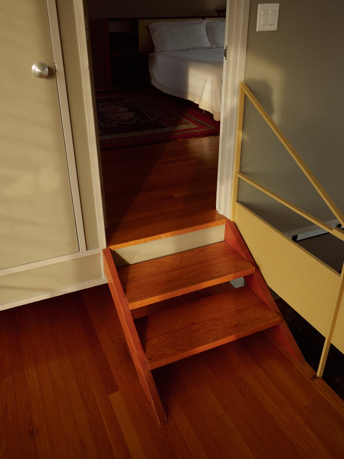 Small wood steps leading through a doorway to the mezzanine bedroom inside the Umbrella House