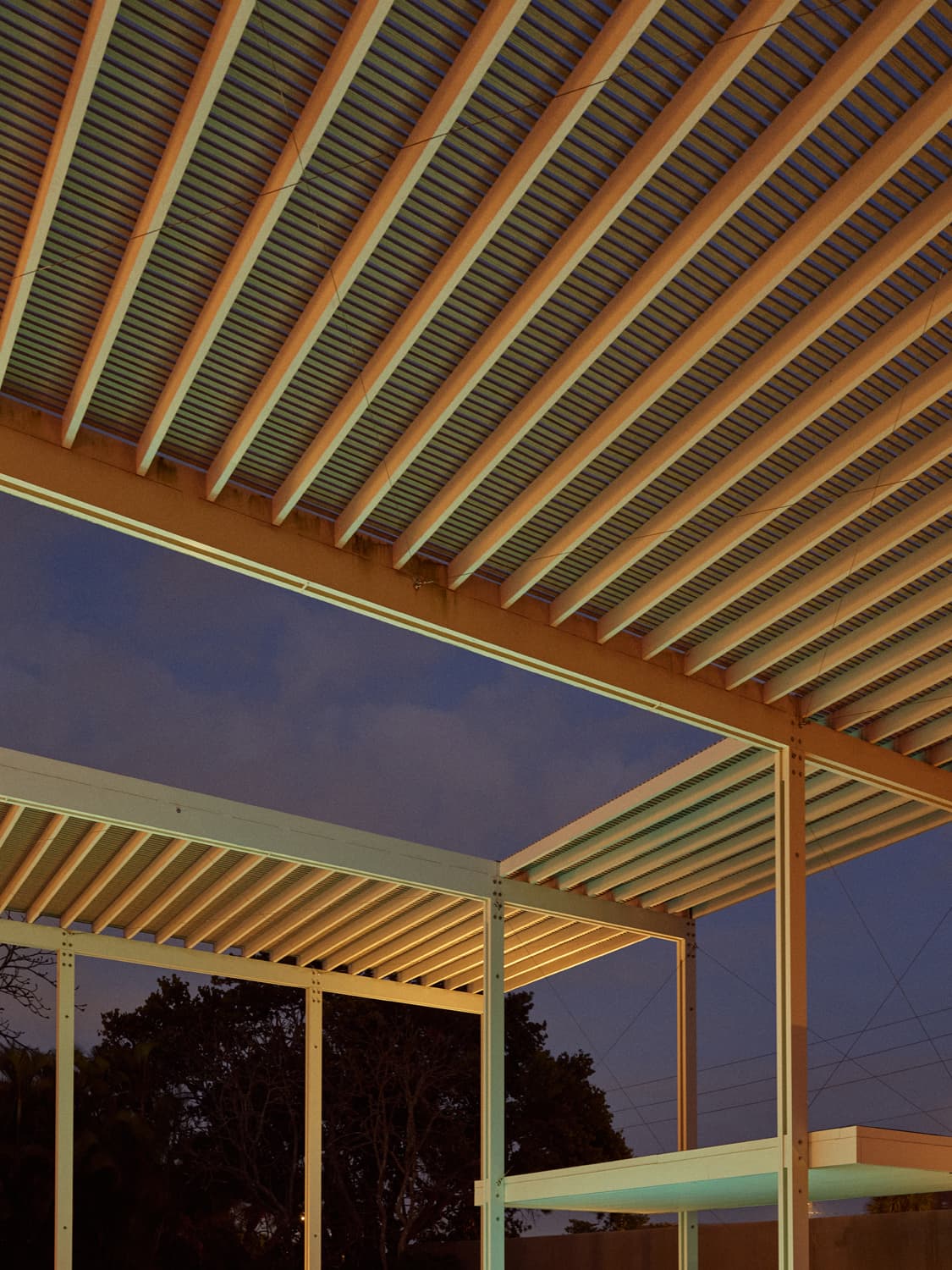 Slatted wood roof beams of the Umbrella House overhang at dusk with blue sky between the slats