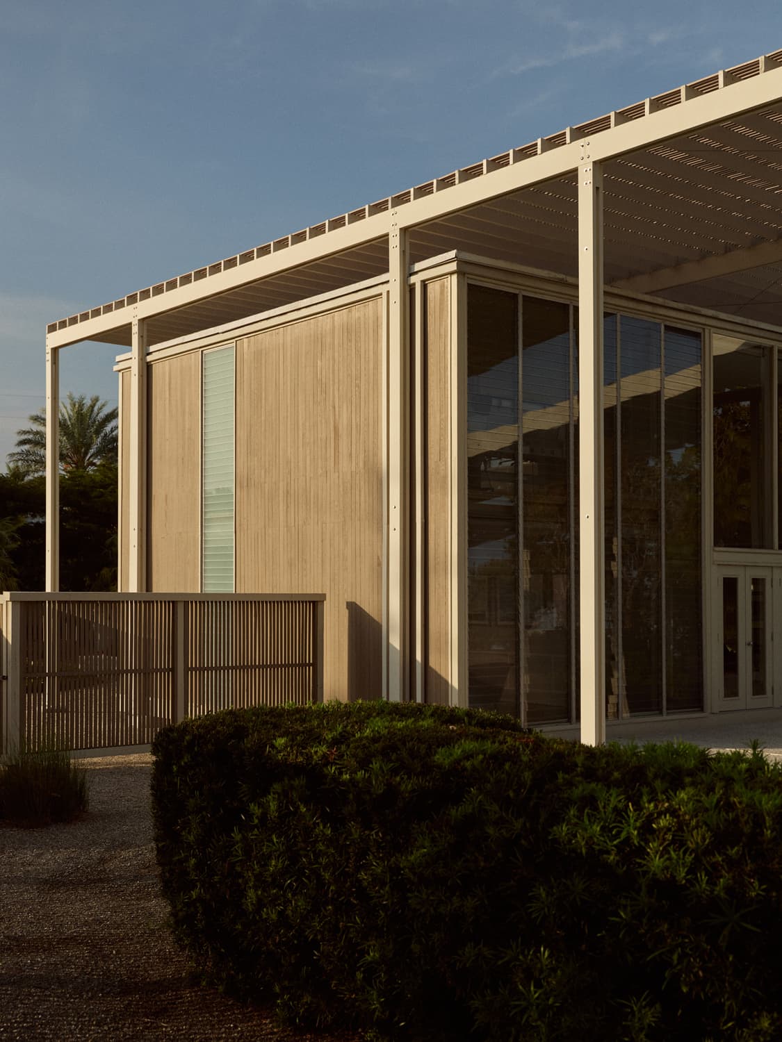 Umbrella House exterior at dusk with slatted overhang, bamboo panels, glass walls, and trimmed hedge