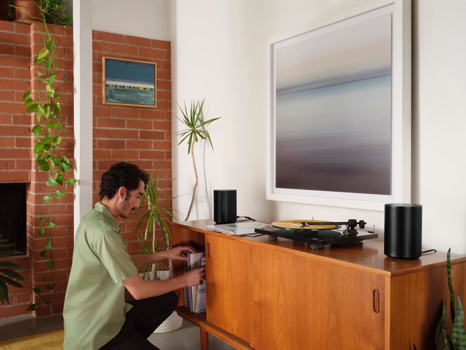 Man browsing vinyl records on a mid-century credenza with Sonos Era speakers