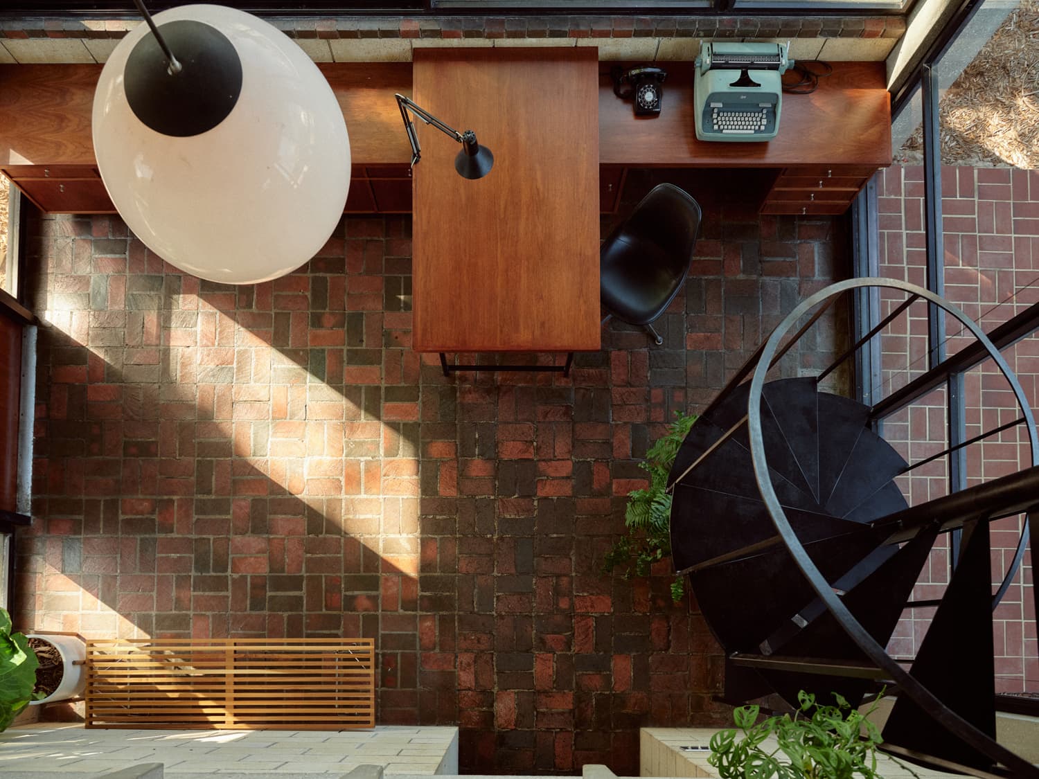 Overhead view of the Strang office with walnut desk, spiral staircase, globe pendant, and brick floor