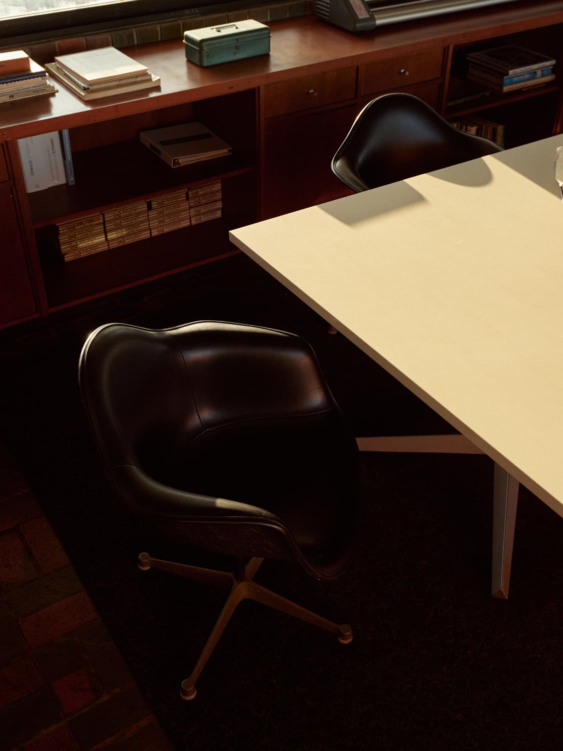Black leather Eames swivel chairs at a white table with walnut credenza in the Strang office