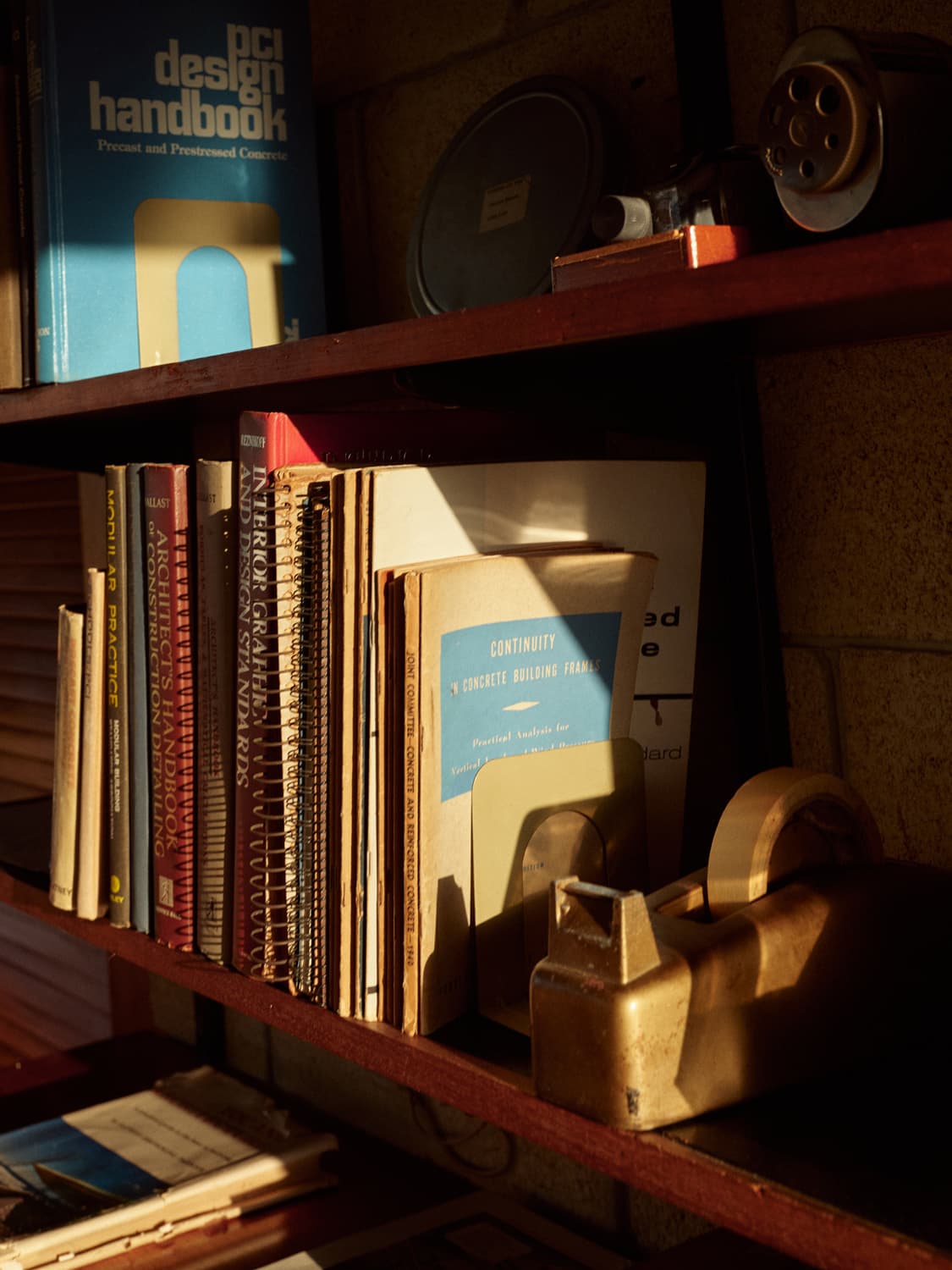 Shelves of vintage architecture reference books and a brass tape dispenser in warm afternoon light