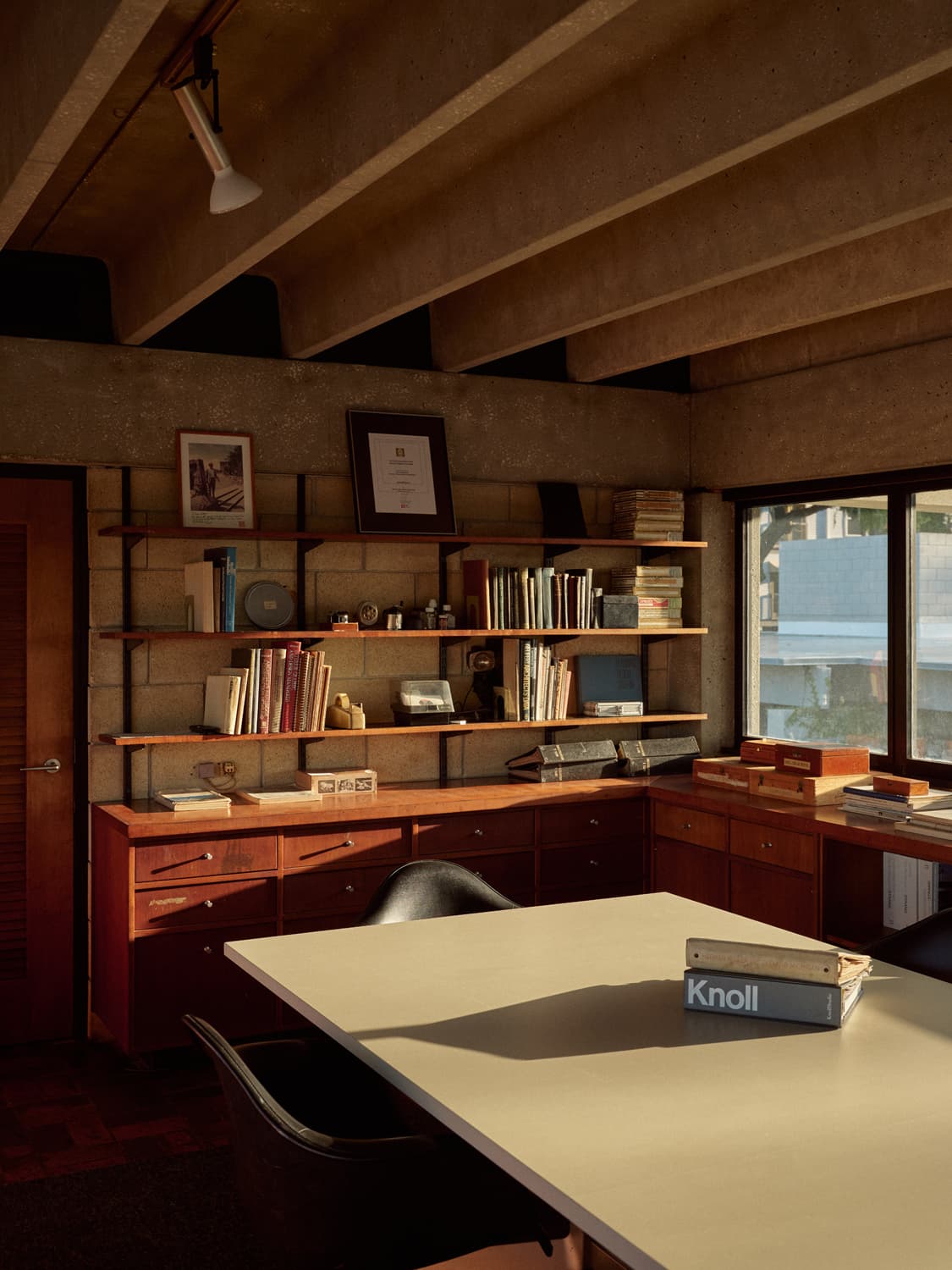 Strang office corner with Knoll catalog on the table, wall shelves, and concrete beam ceiling