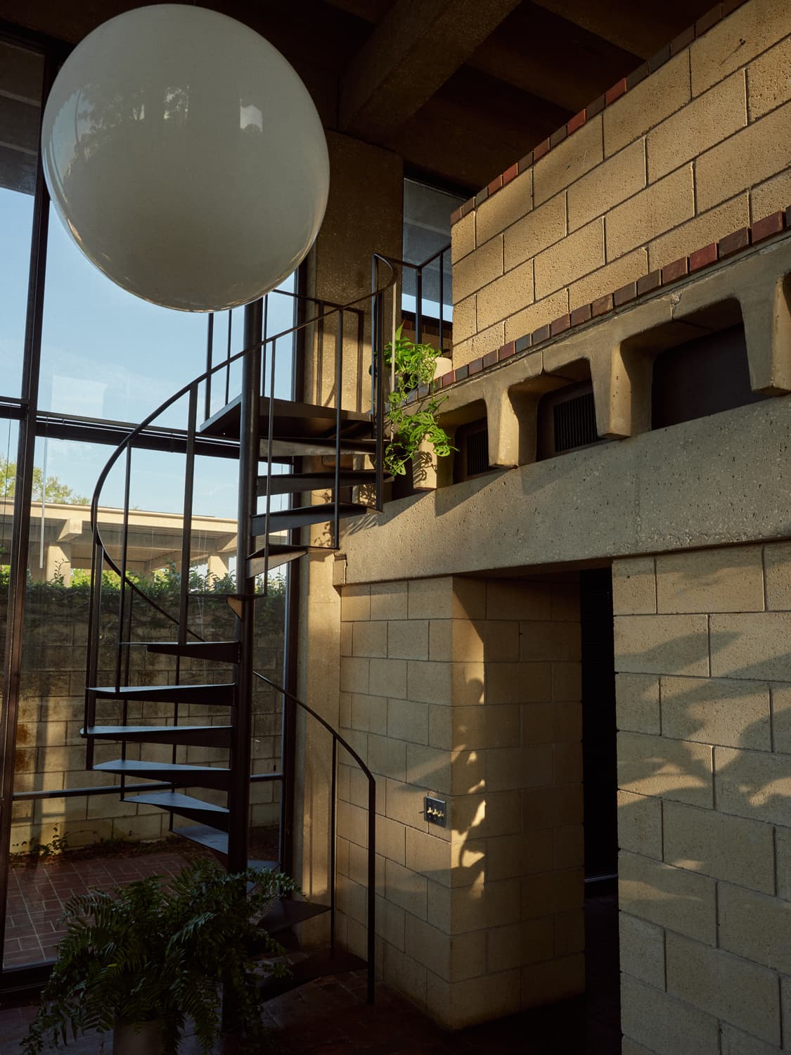 Spiral staircase and globe pendant light inside the double height concrete block entry of Strang office